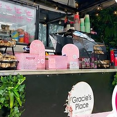 The Gracie's Place van counter stacked with pink cups and snacks, with greenery underneath